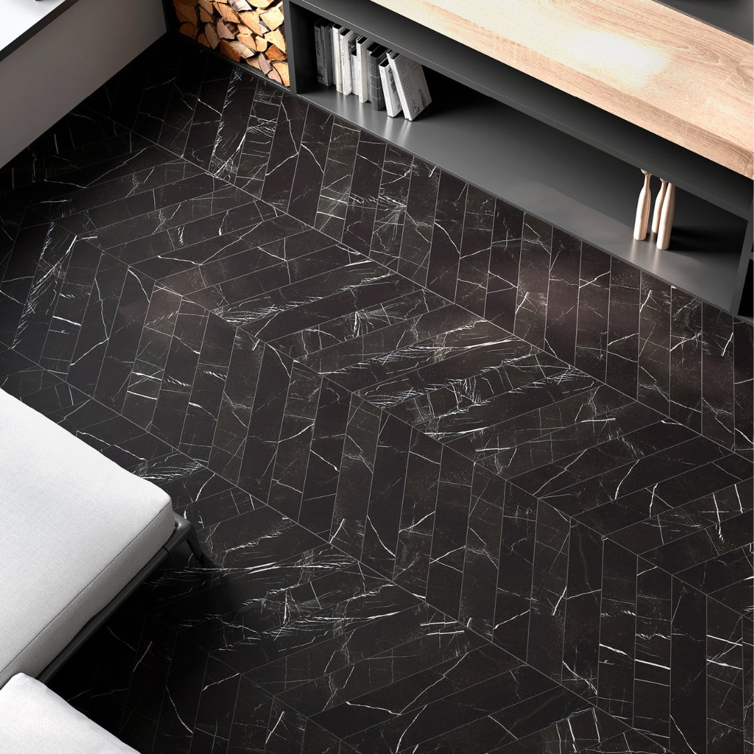 Ariel view of a living space floor with white. black and wood elements surrounding the tile installation. The tiles are matte black with white marble-like veining and they are in a 4x20 chevron format. the chevron installation allows much more marble pattern veining for a maximal visual interest. 