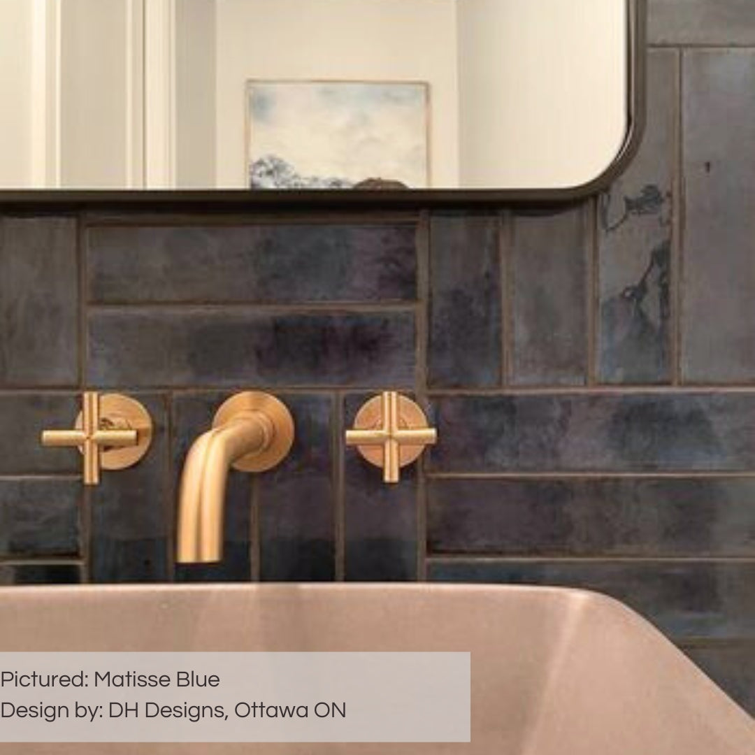 a close up of the matisse blue glossy subway tiles installed on a bathroom backsplash with a gold faucet. 