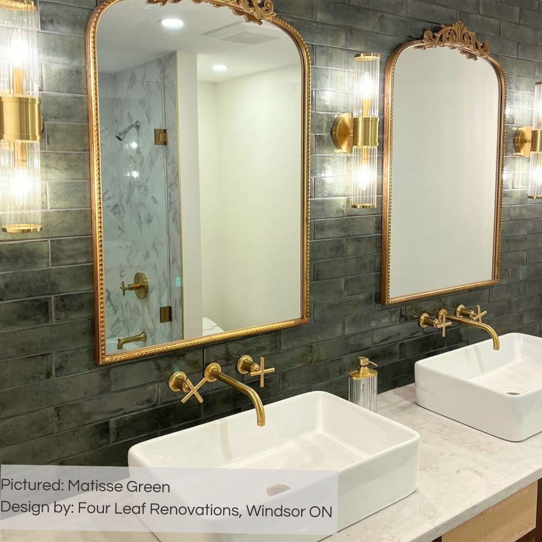 A glamorous fusion bathroom with double vanity and vintage style mirrors with matisse green tiles installed on the backsplash in a traditional brick layout. 