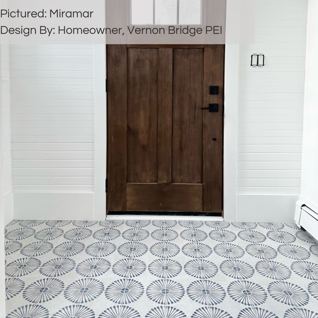 A fun pattern entry way floor using miramar 8x8 flower pattern blue and grey tiles. the door is a rich wood and the walls are white. 