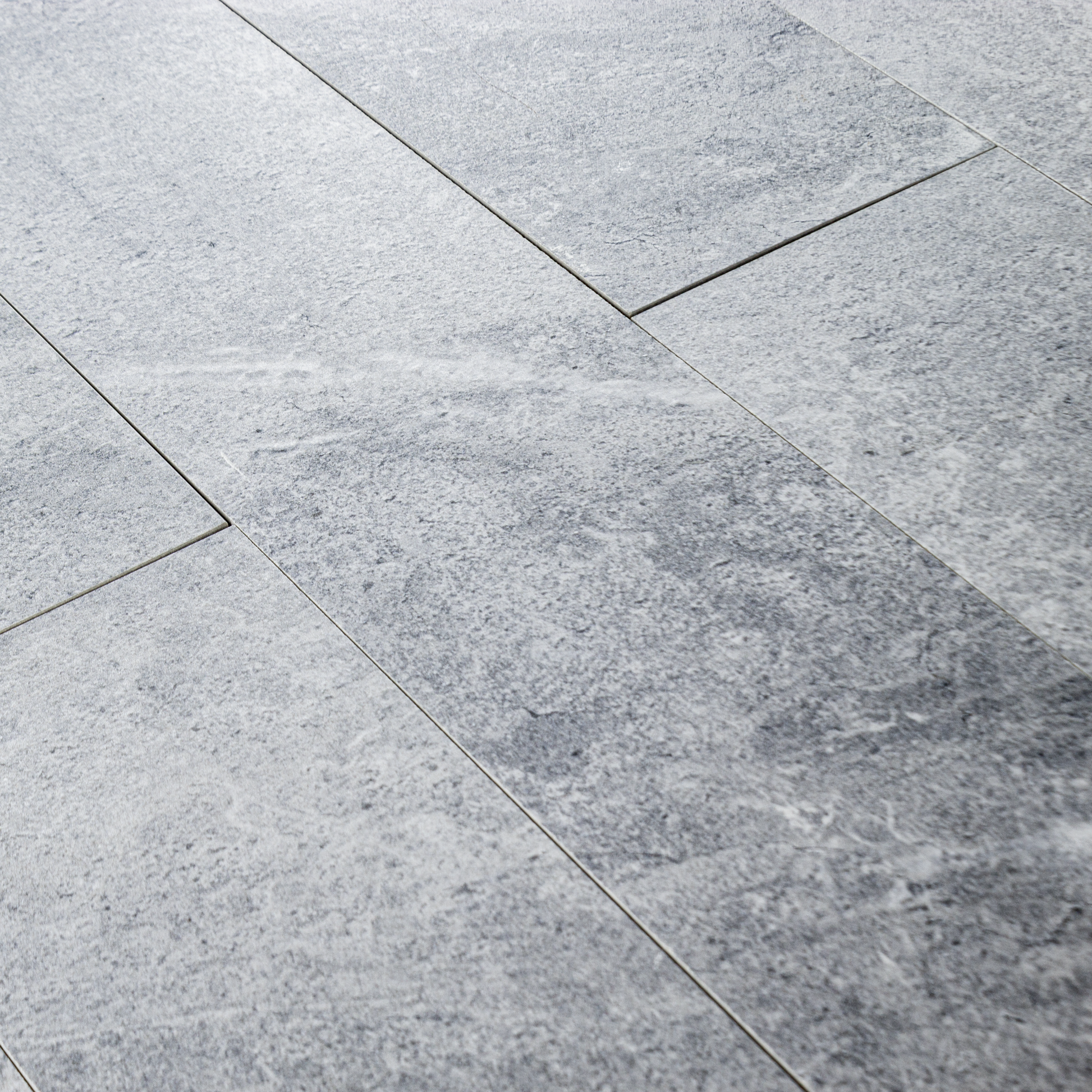 Angled close up of a group of 4x24 light grey stone look tiles in a brick layout. 