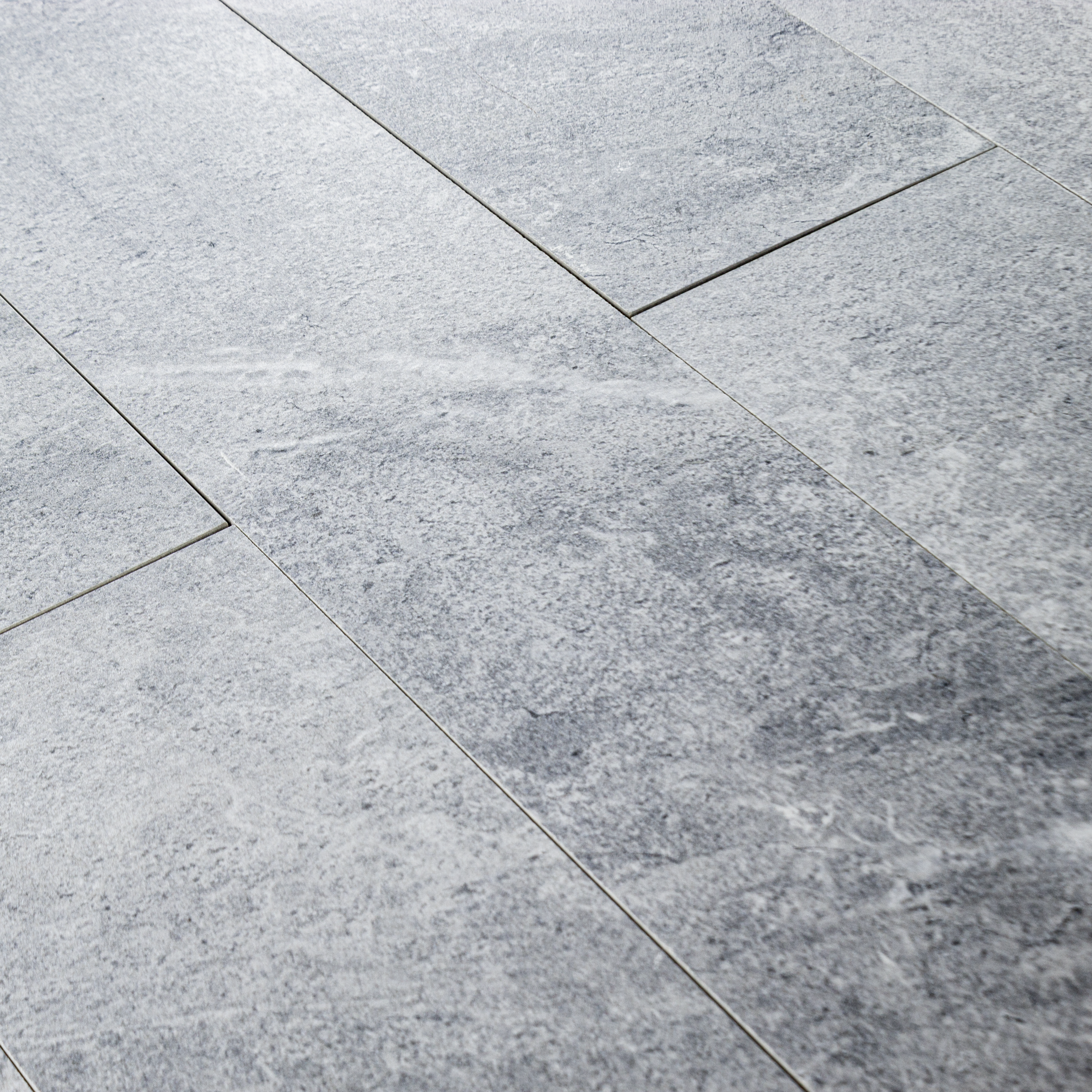 Angled close up of a group of 4x24 light grey stone look tiles in a brick layout. 
