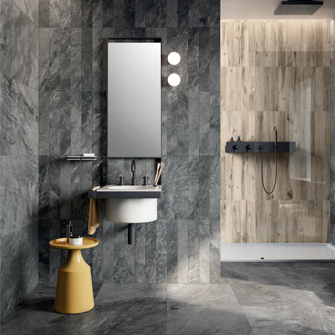 A modern bathroom with 24x48 dark grey stone look tiles installed on the floors of the bathroom in a vertical stack. The same tile is used on the bathroom walls in another size for a cohesive modern look. 
