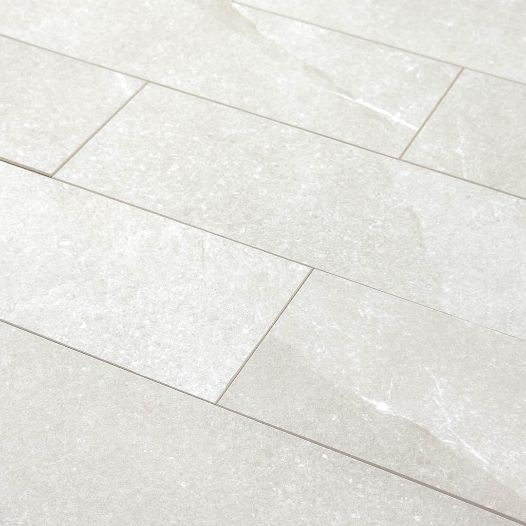 Angled close up of a group of stone look 4x12 matte tiles in light grey laid out in a brick pattern to show the pattern, finish and variance.