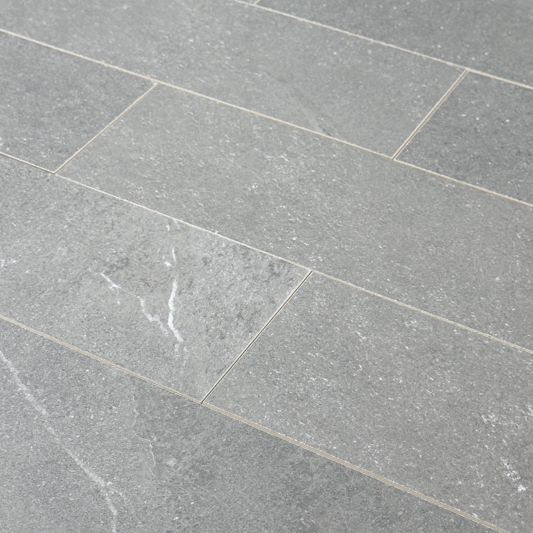 Angled close up of a group of limestone look 4x12 matte tiles in dark grey laid out in a brick pattern to show the pattern, finish and variance.