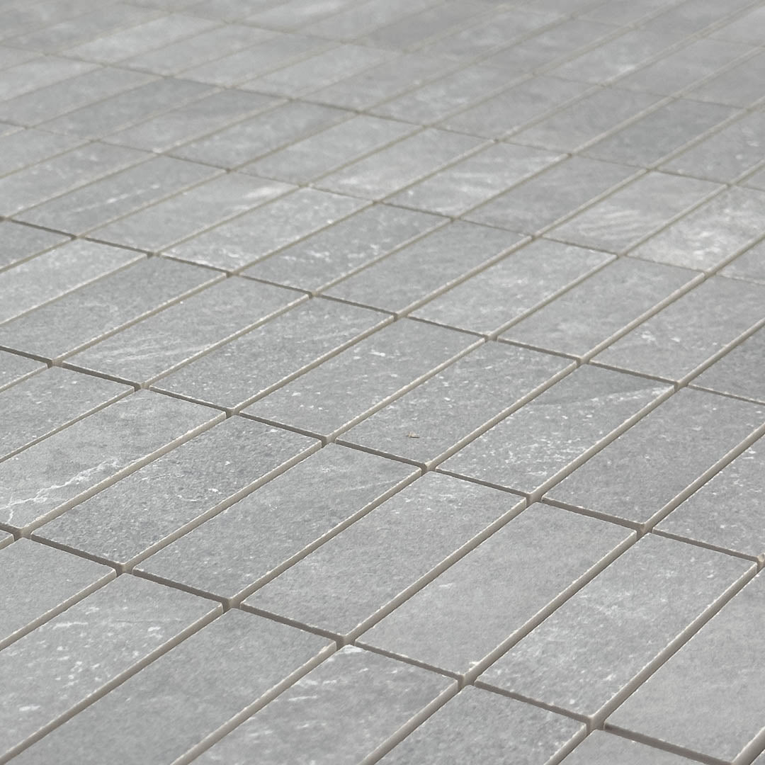 Angled close up view of a mosaic dark grey stone look tile in a stacked chip shape 1x3 where the subtle stone pattern and matte finish are highlighted. 