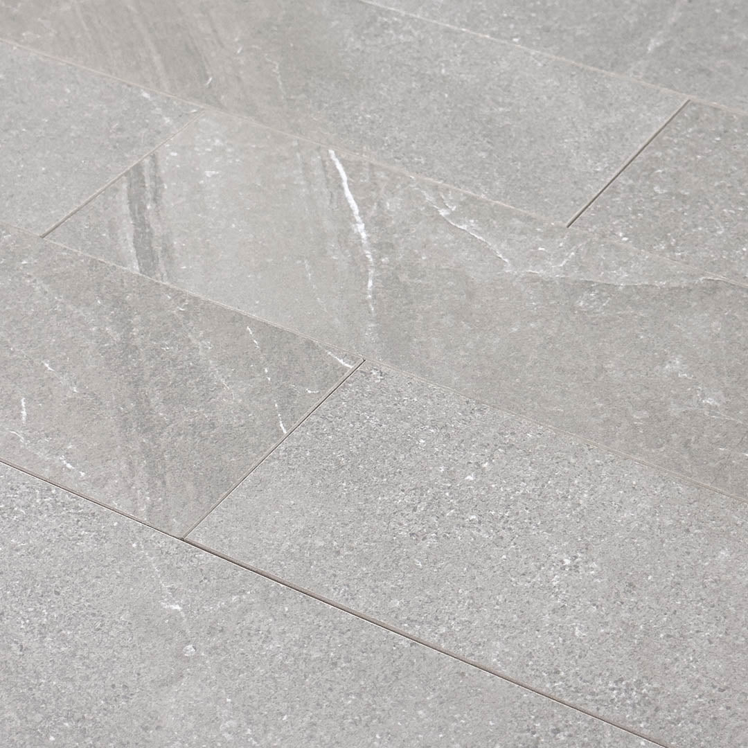 Angled close up of a group of limestone look 4x12 matte tiles in taupe laid out in a brick pattern to show the pattern, finish and variance.