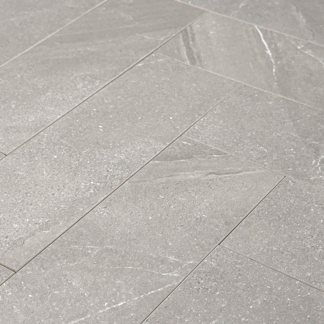 Angled close up of a group of limestone look 4x12 taupe matte tiles laid out in a herringbone pattern to show the pattern and finish.