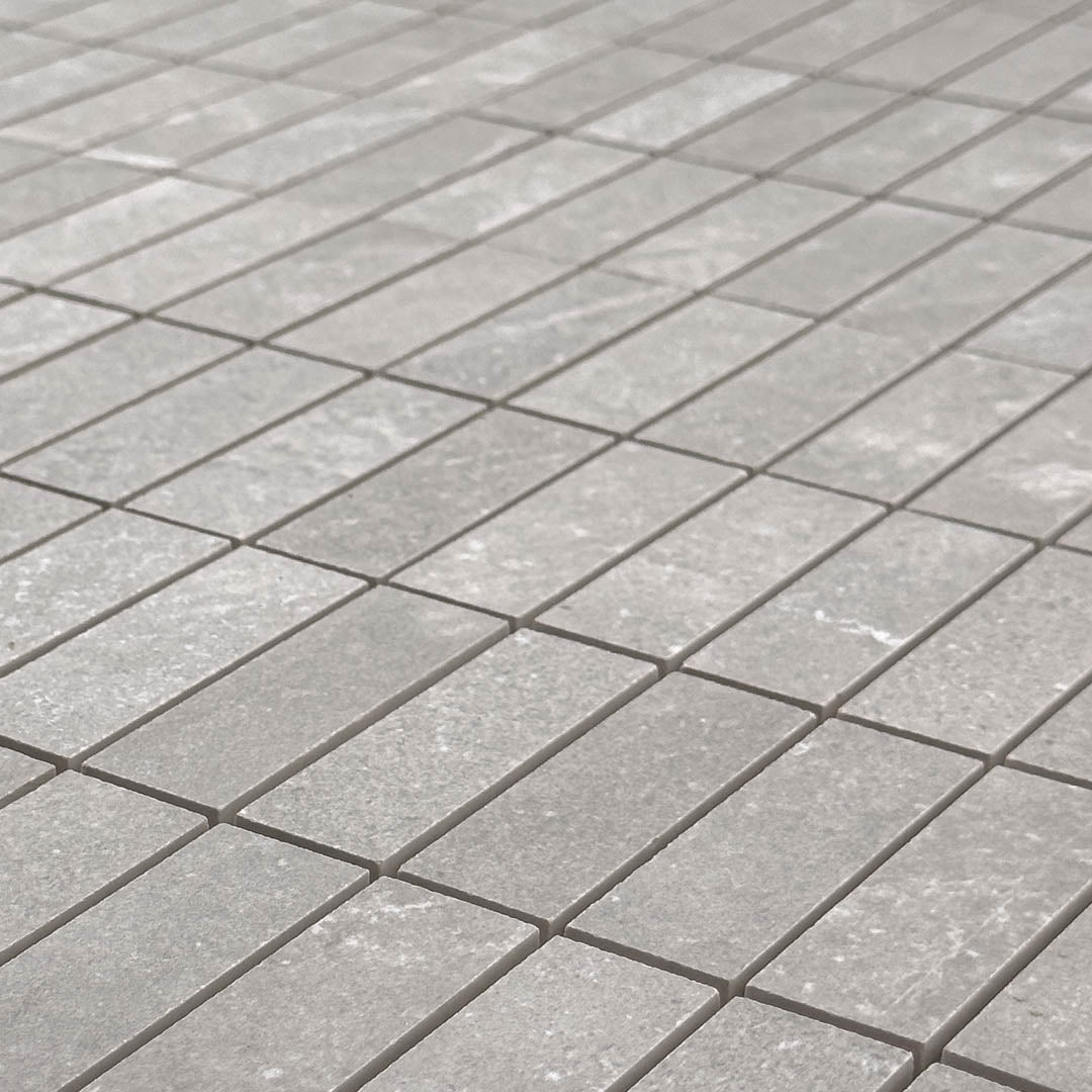 Angled close up of limestone look mosaic tile in taupe with light veining pattern and a matte natural finish that is a modern stack pattern. 
