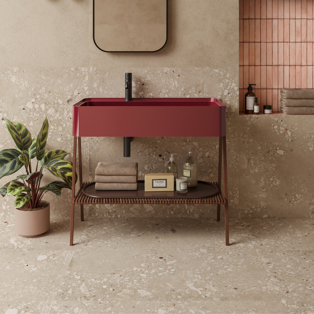 A warm washroom with natural accents and 36x36 cement terrazzo look tiles in a sandy dark colourway. the tiles are installed on the floors and halfway up the wall to provide backsplash for the sink. there are brown, red and pink accents. 