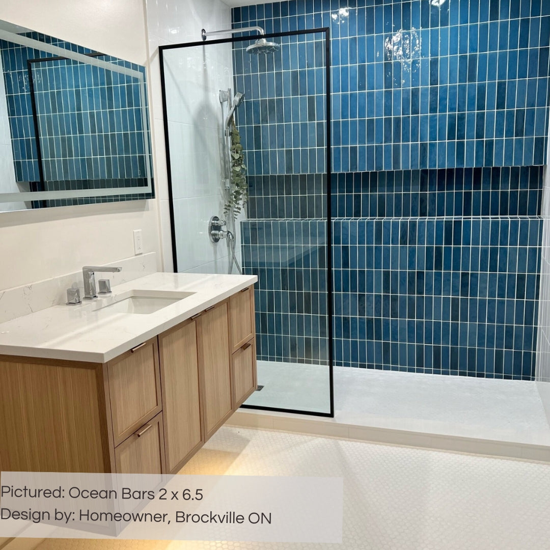 A tiled shower wall featuring 2x6.5 ocean bars; a glossy cobalt sapphire blue tile with heavy colour variation. The other finishes are bright white and the vanity is light wood. 
