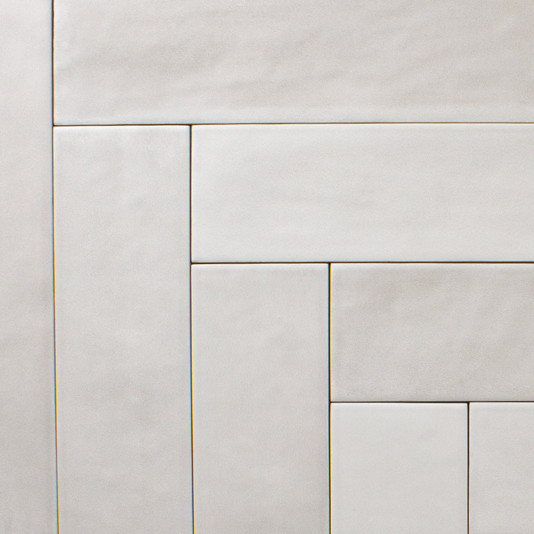 An ariel view of 2x9 matte subway tiles in a light grey shade with subtle texture. Laid out in a herringbone pattern. 