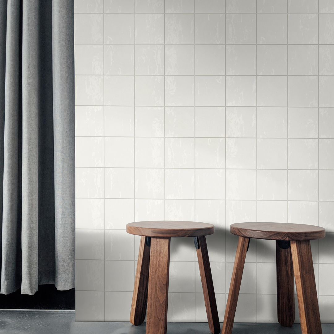 A close up of a wall outside of a walk in shower with two wooden stools. The wall features 5x5 glossy white zellige tiles. 
