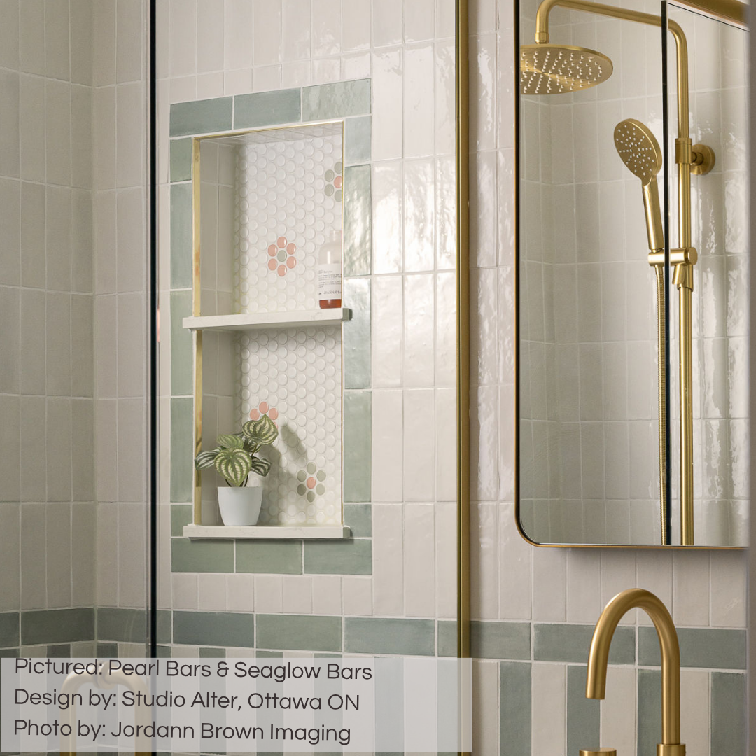 A bathroom wall and shower tile installation with gold accents. The tiles are glossy pearl white that catch the light with their texture. The white tiles are in a vertical stack on the upper half of the wall, and in a vertical coastal stripe on the lower half mixed with seaglow green tiles. 