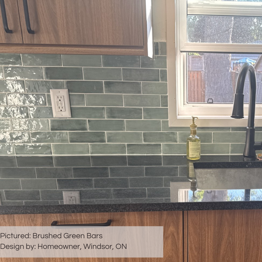A close up of a kitchen green subway tile backsplash using brushed green bars. the tiles have a colour variation in a glossy finish. they are surrounded by medium brown wood cabinets and a black countertop. 