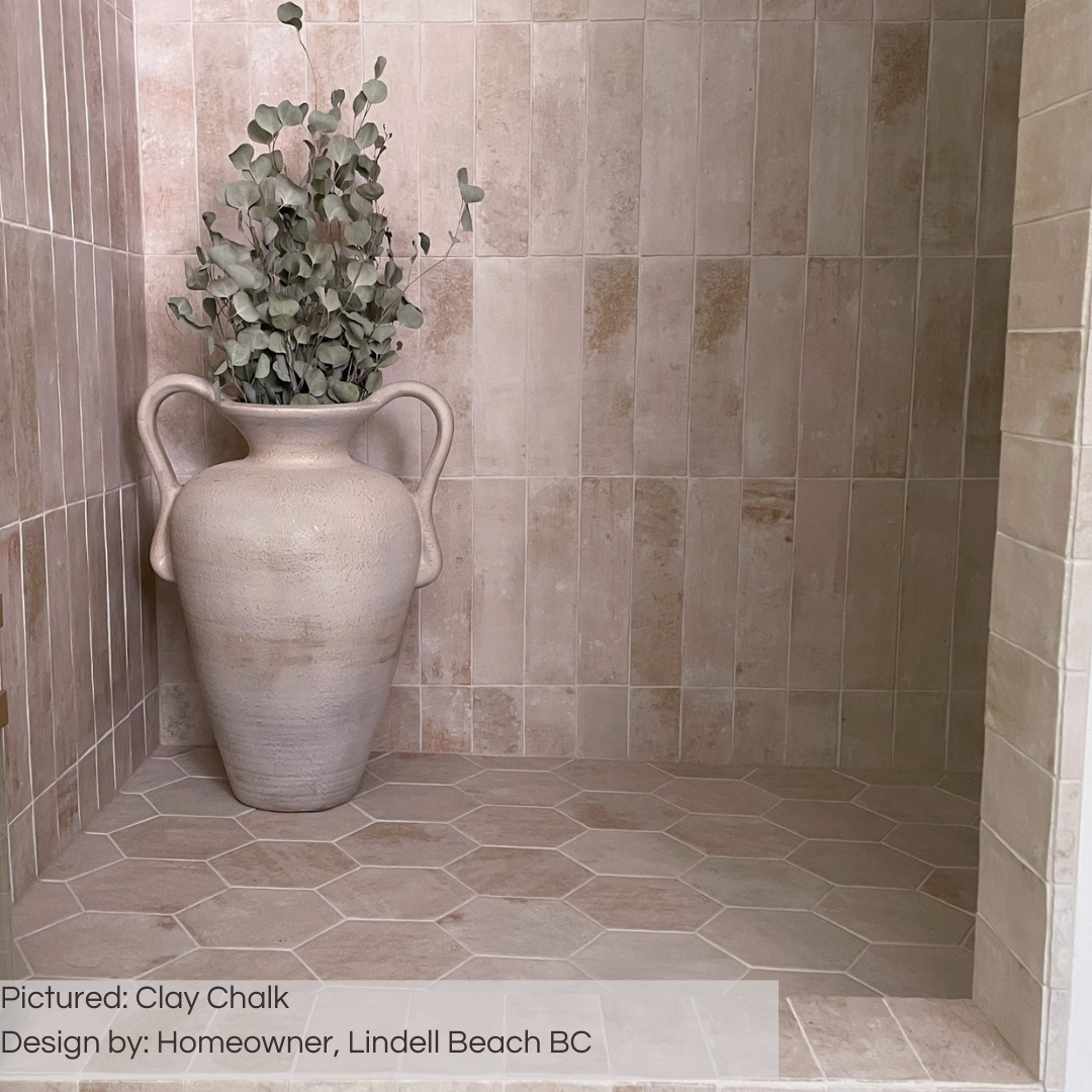 An earthy vibe walk in shower with clay chalk 6" hexagon tiles on the shower floor and the same matching coordinating tile in 11x2.75 in a vertical stack for the walls. This shower looks as timeless as ever and cohesive using the same variated shade tiles in different sizes. 