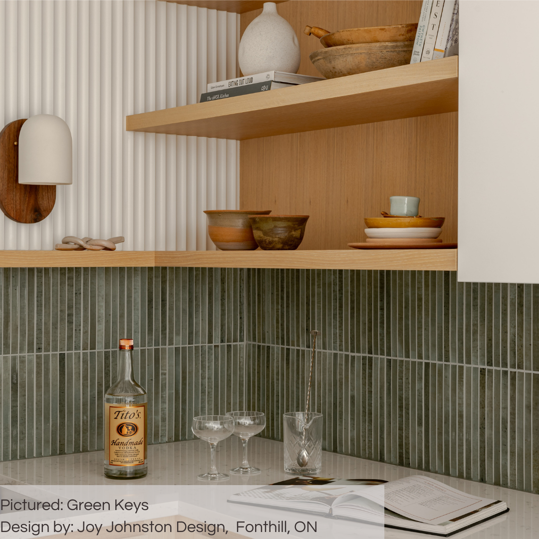 A close up of a modern kitchen backsplash with wood open shelving in place of upper cabinets. Below the lowest shelf are the green keys 5x10 fluted tiles with a light grey grout to highlight each kitkat piece. the countertop matches the grout. 