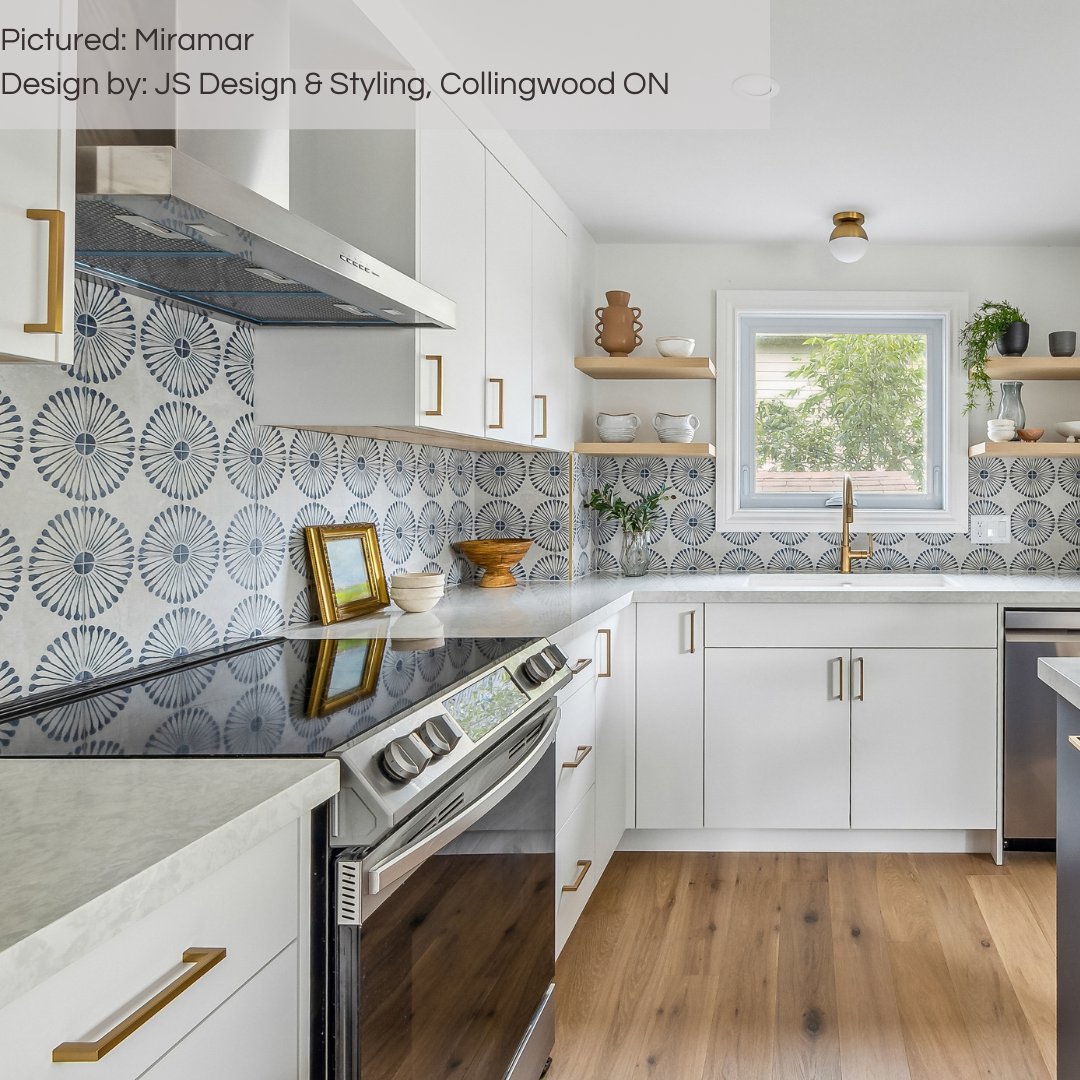 A white modern kitchen with gold and light wood accents, a backsplash using miramar blue and grey sunburst flower pattern tiles. 