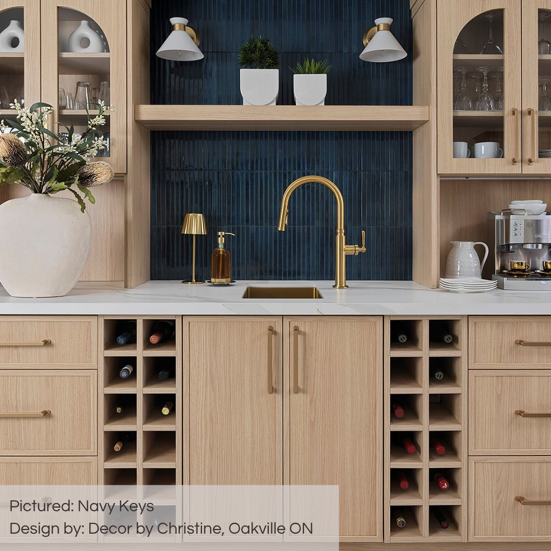 A stunning coffee bar with light oak upper and lower cabinets, with a white counter and gold hardware. the tiled backsplash is navy blue keys fluted glossy kitkat tiles. 