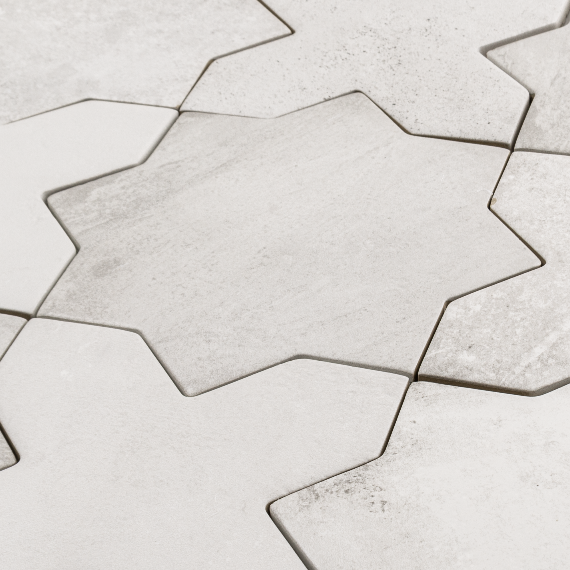 Angled close up of a group of star and cross shaped tiles interlocking together in a matte white colour variated finish. 