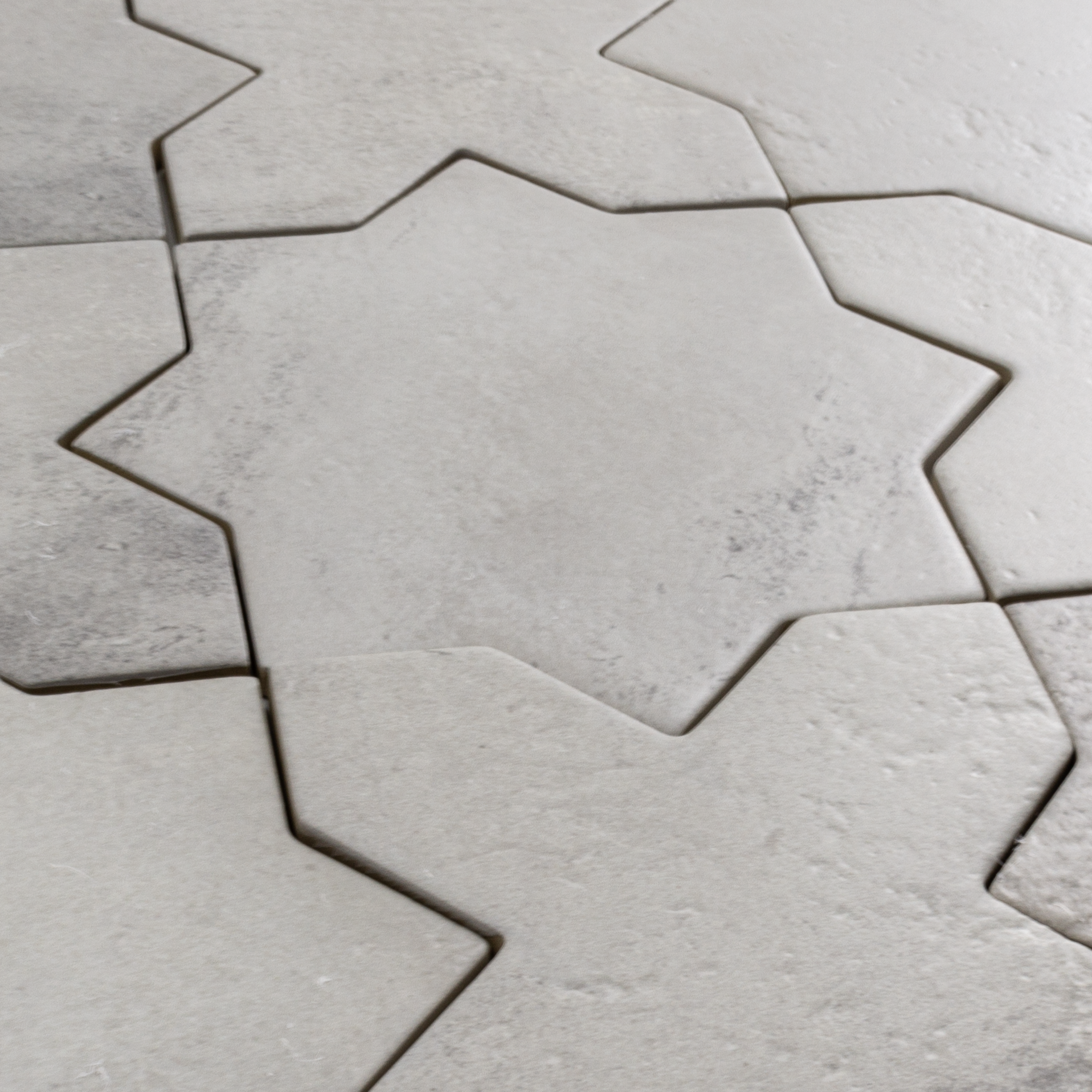 Angled close up of a group of star and cross shaped tiles interlocking together in a matte grey stone look finish