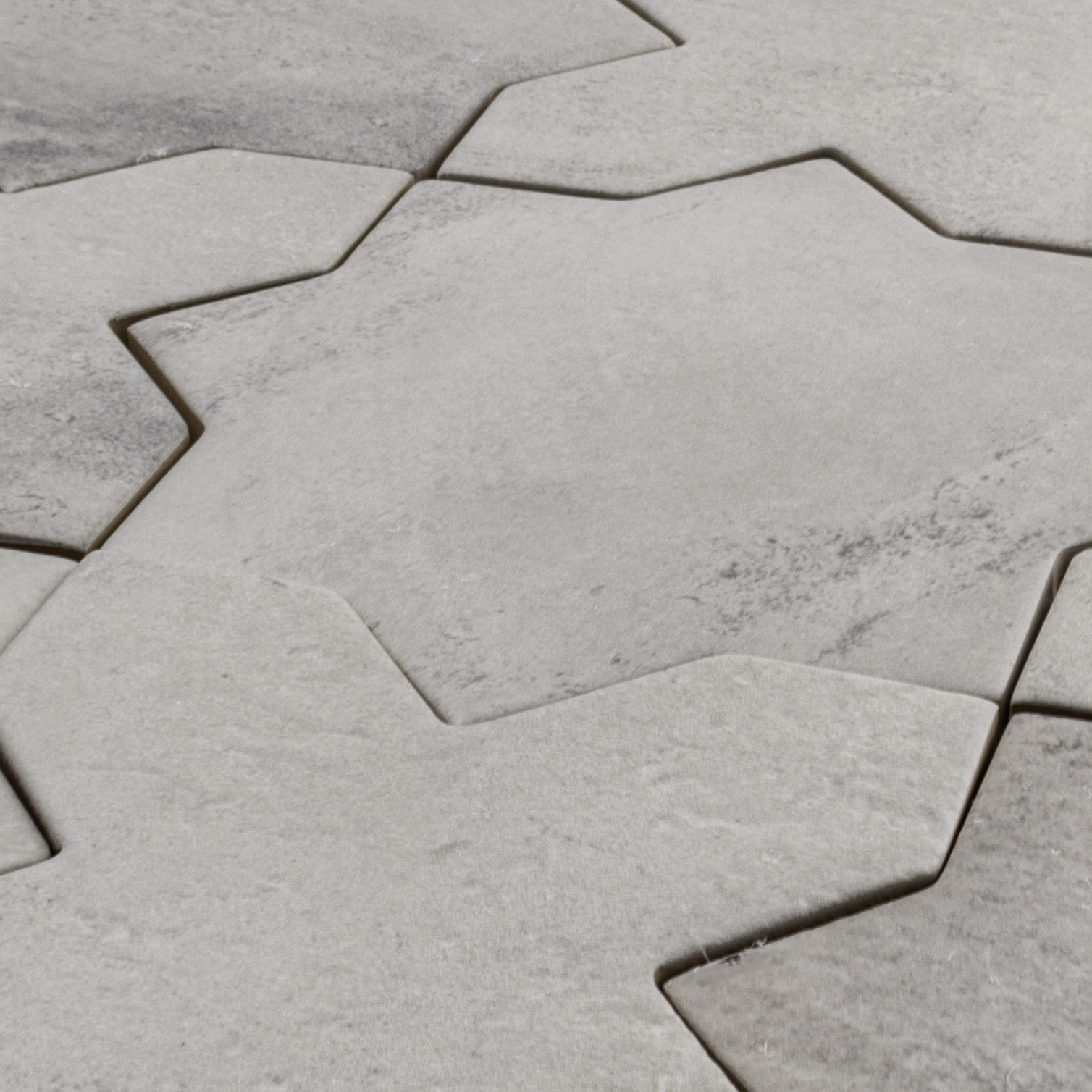 Angled closer look of a group of star and cross shaped tiles interlocking together in a matte grey stone look finish highlighting the pattern and colour variance. 