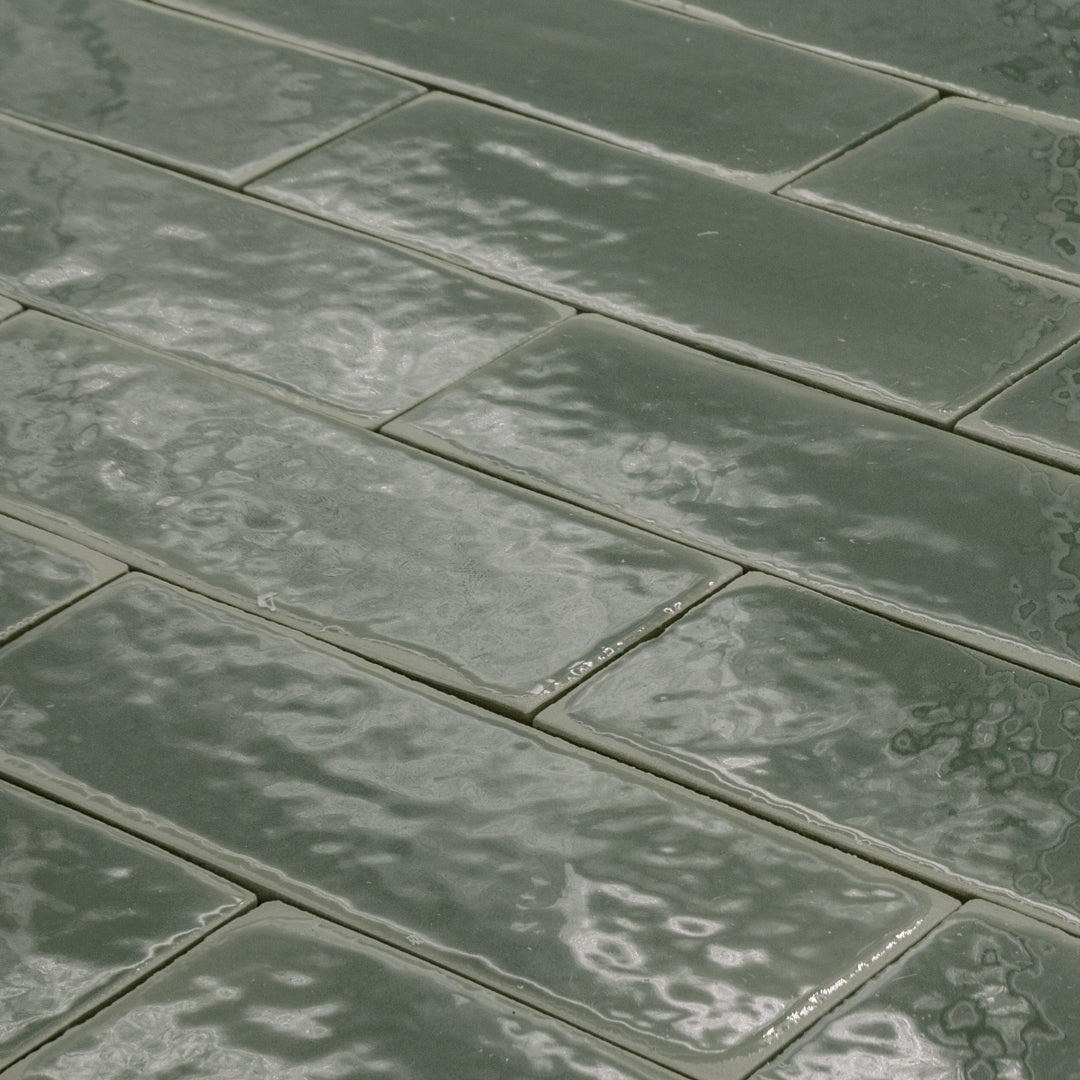 angled view of a group of dark moss fir green 2x6 glossy subway tiles with a soft texture and uneven edges in a brick layout. 