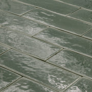 angled view of a group of dark moss fir green 2x6 glossy subway tiles with a soft texture and uneven edges in a brick layout. 