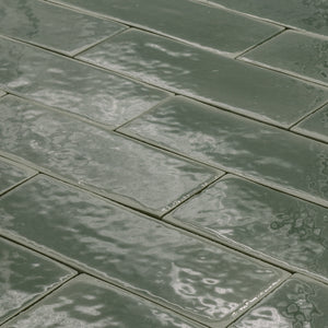 angled view of a group of dark moss fir green 2x6 glossy subway tiles with a soft texture and uneven edges in a brick layout. 