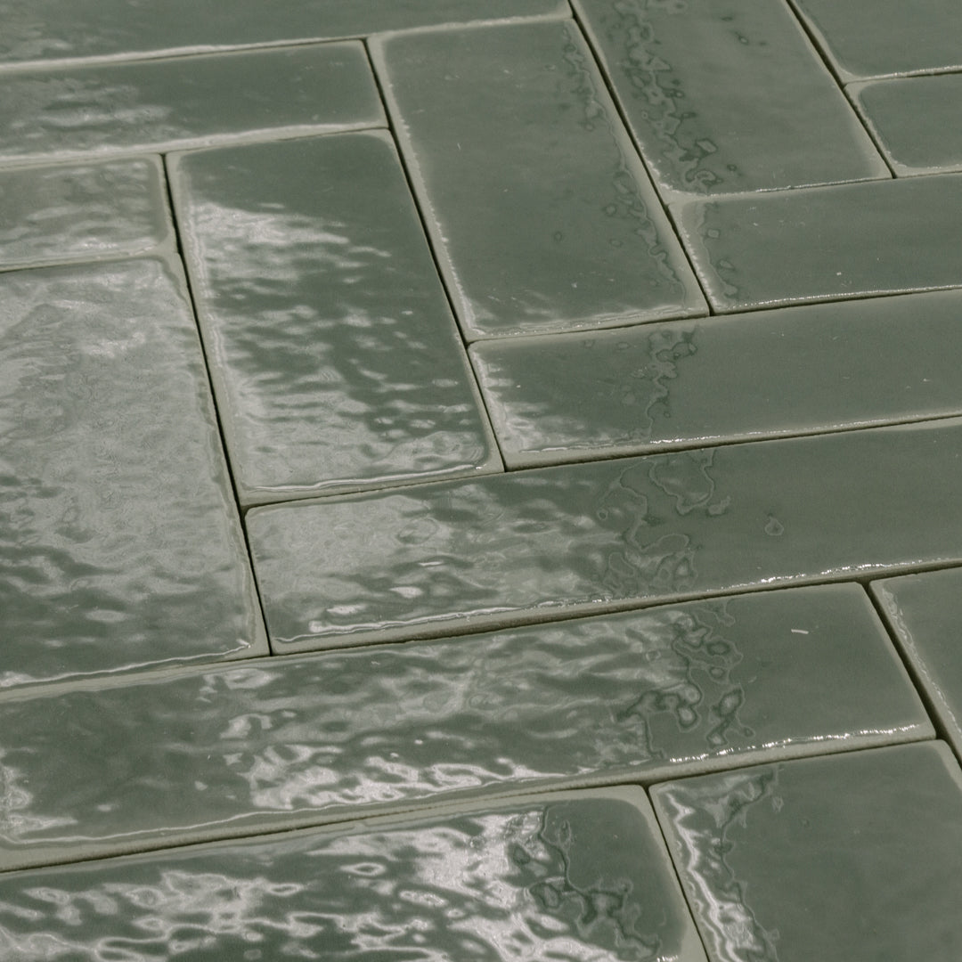 a group of dark moss fir green 2x6 glossy subway tiles with a soft texture and uneven edges in a herringbone layout. 
