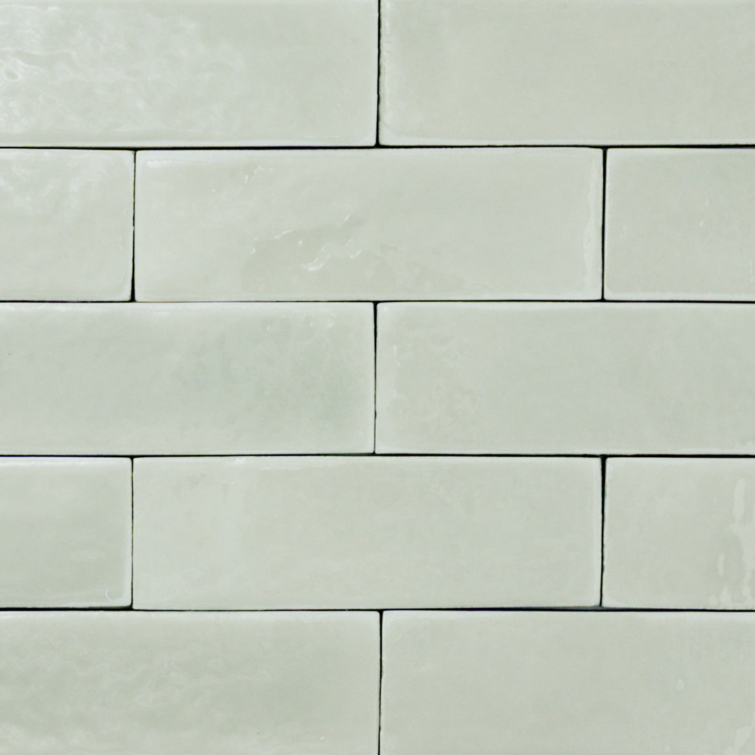 a group of light green sage 2x6 glossy subway tiles with a soft texture and uneven edges in a brick layout. 