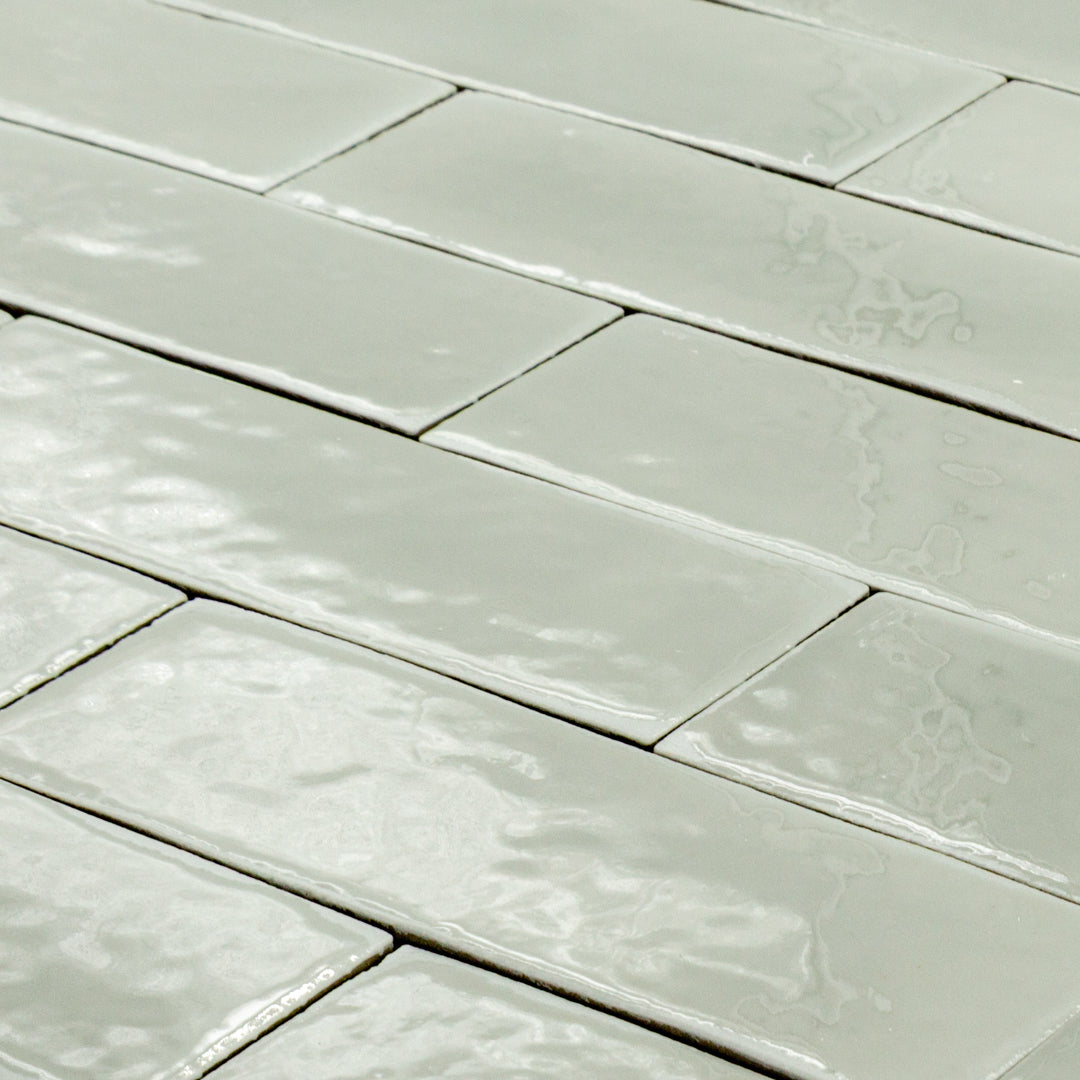 angled view of a group of light green sage 2x6 glossy subway tiles with a soft texture and uneven edges in a brick layout. 