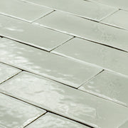 angled view of a group of light green sage 2x6 glossy subway tiles with a soft texture and uneven edges in a brick layout. 