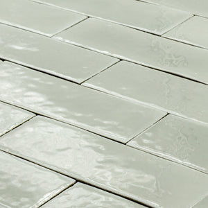 angled view of a group of light green sage 2x6 glossy subway tiles with a soft texture and uneven edges in a brick layout. 