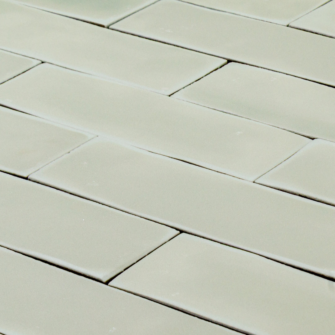 angled view of a group of light green sage 2x6 matte subway tiles with a soft texture and variance in a brick layout. this angle shows the uneven edges of tile for texture. 