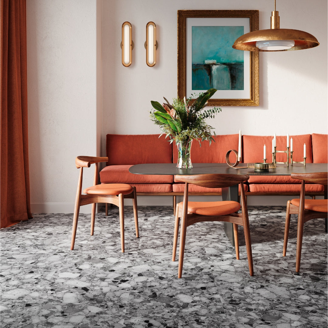 A floor application of the Rainstone Granite terrazzo look porcelain tiles showing the light grey and dark grey shades. The flooring is in a dining room or breakfast nook with oranges, wood and gold accents. 
