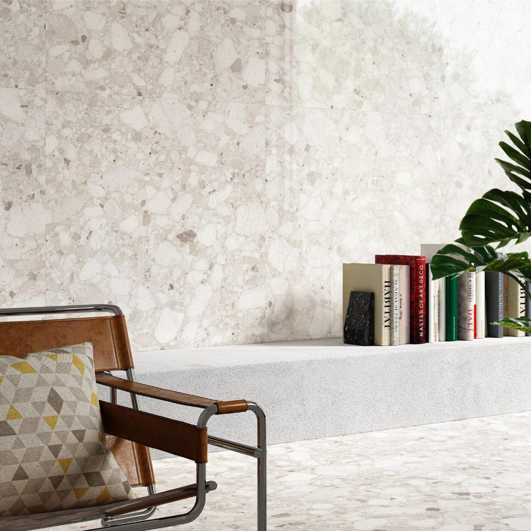 A wall and floor application using offwhite Rainstone powder terrazzo look tiles. There are some beige and grey shades throughout. A blended look of natural vibes with a concrete slab book nook and modern leather and metal chair. 