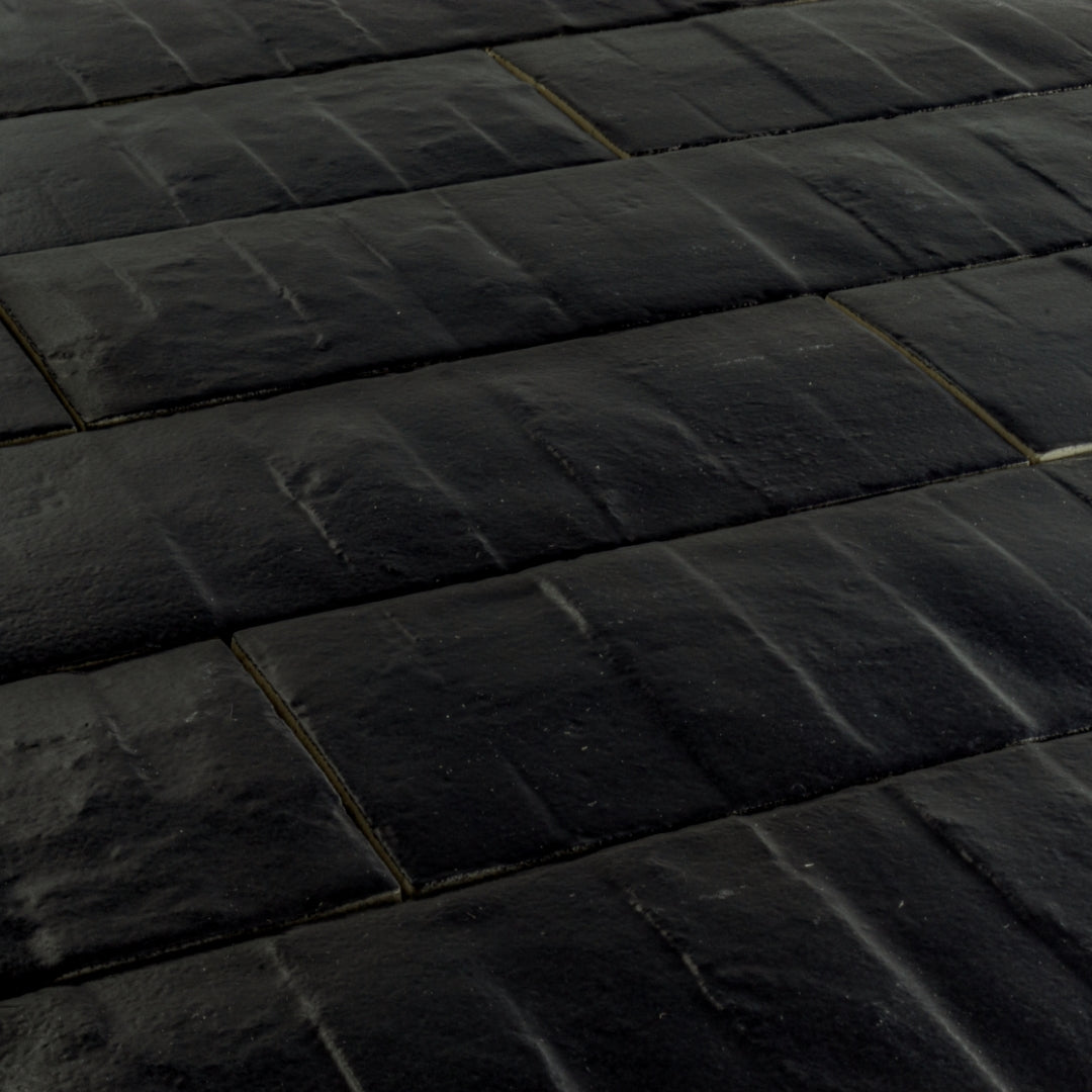 Angled close up view of 3x12 rich black textured tiles arranged in a brick layout. 