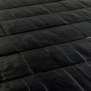 Angled close up view of 3x12 rich black textured tiles arranged in a brick layout. 