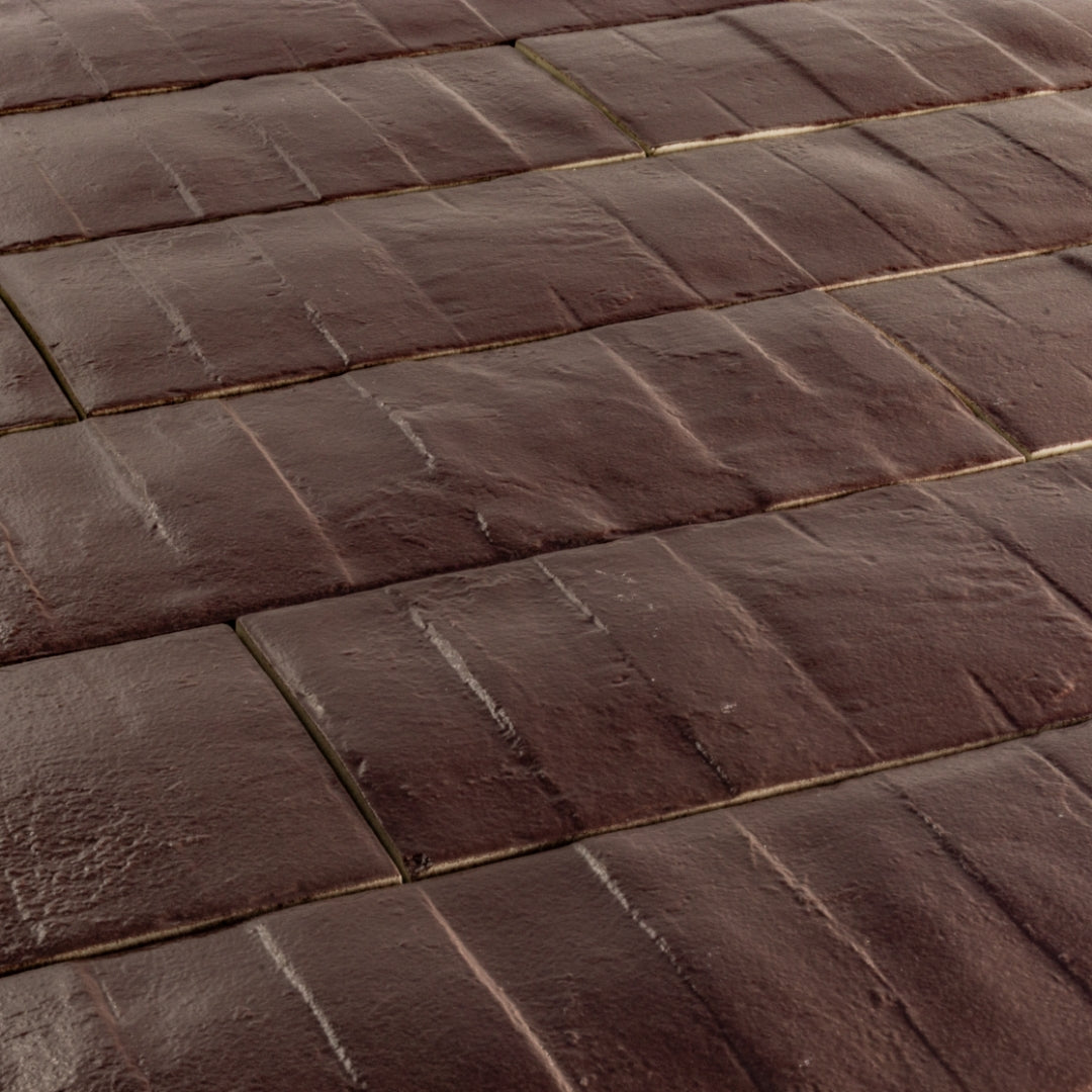 Angled close up view of 3x12 burgundy textured tiles arranged in a brick layout. 