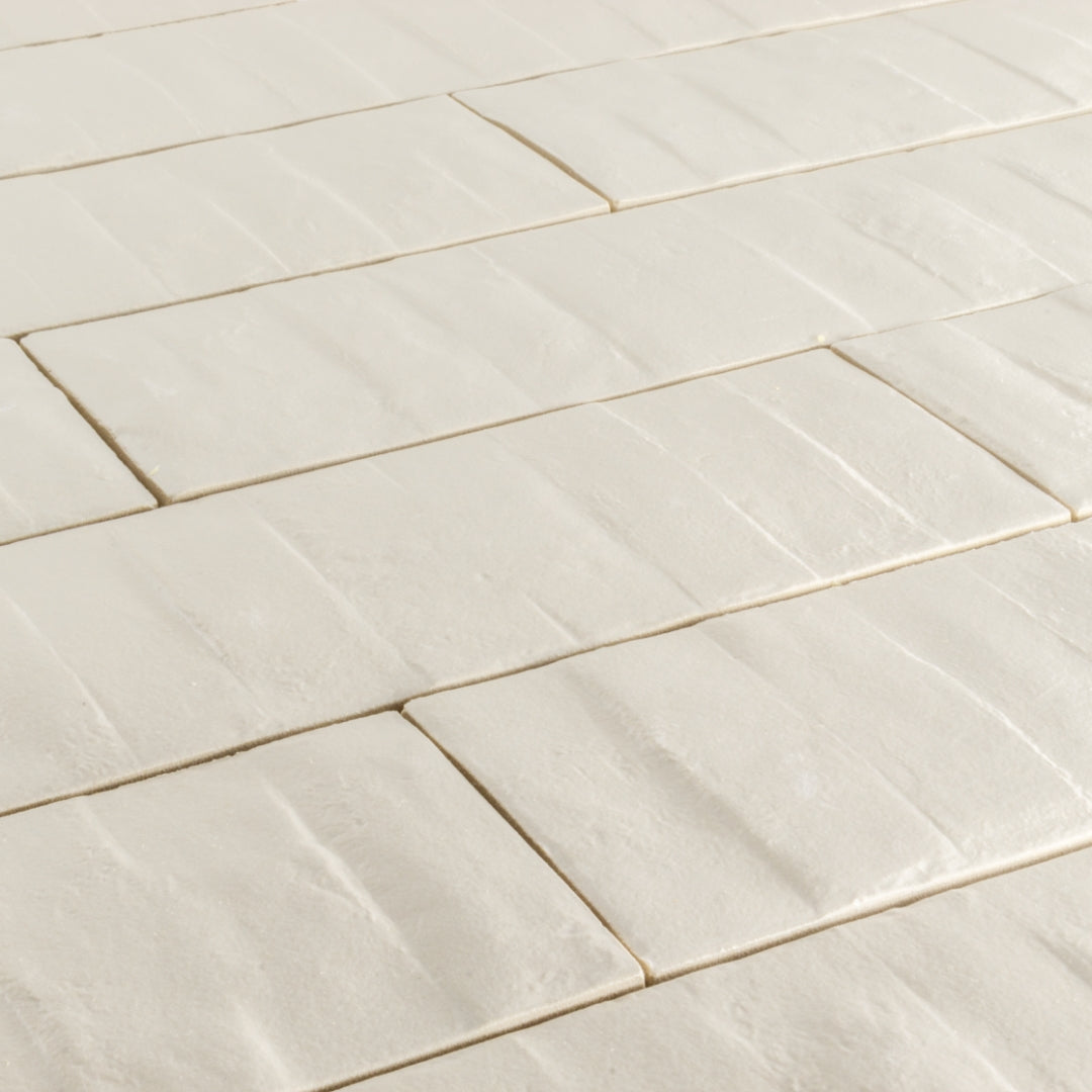 Angled close up view of 3x12 off white beige textured tiles arranged in a brick layout. 