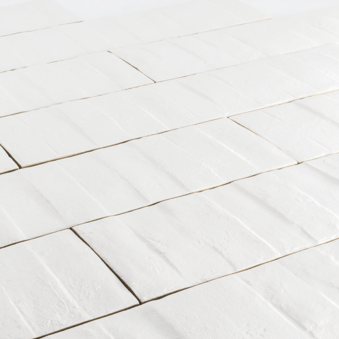 Angled close up view of 3x12 white textured tiles arranged in a brick layout. 