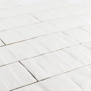 Angled close up view of 3x12 white textured tiles arranged in a brick layout. 