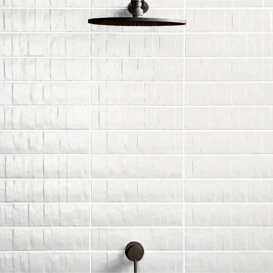 A close up of a textured tile in a shower. The tiles are white and have lots of texture to catch the light, and the tiles are installed in a modern horizontal stack. 