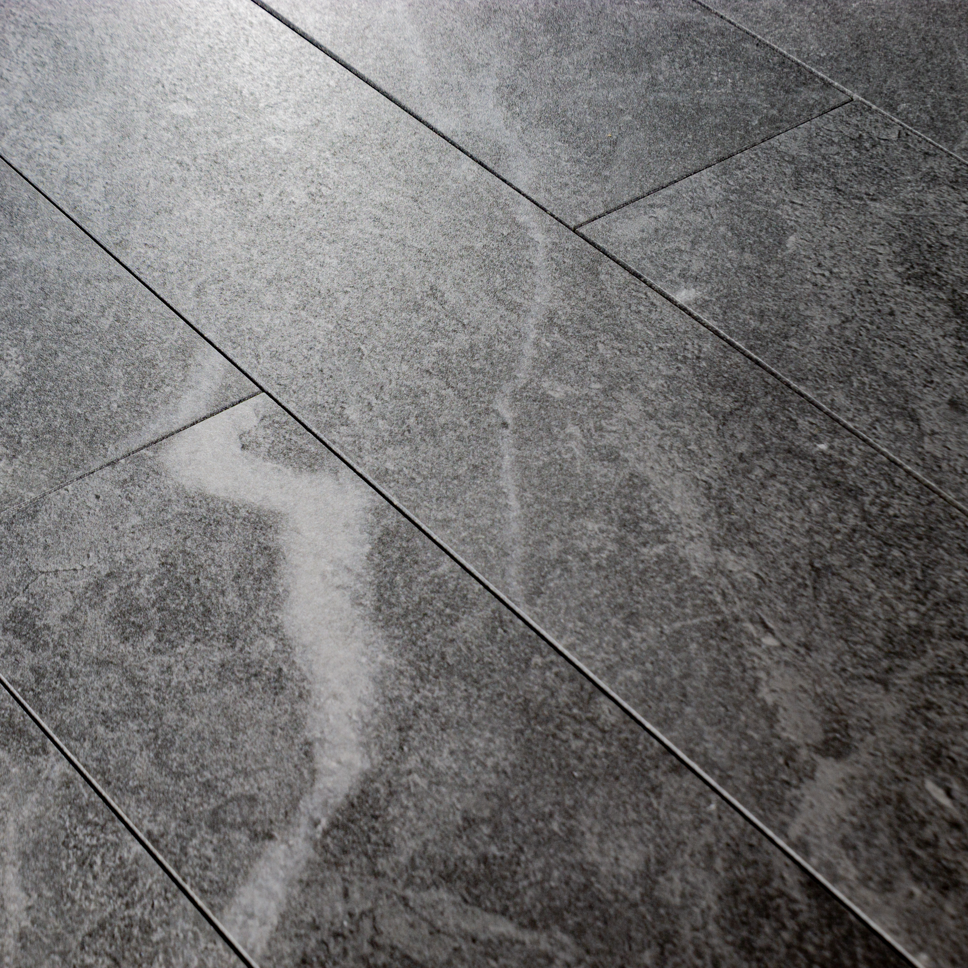 Angled close up of a group of 4x24 dark grey stone look tiles in a brick layout. 