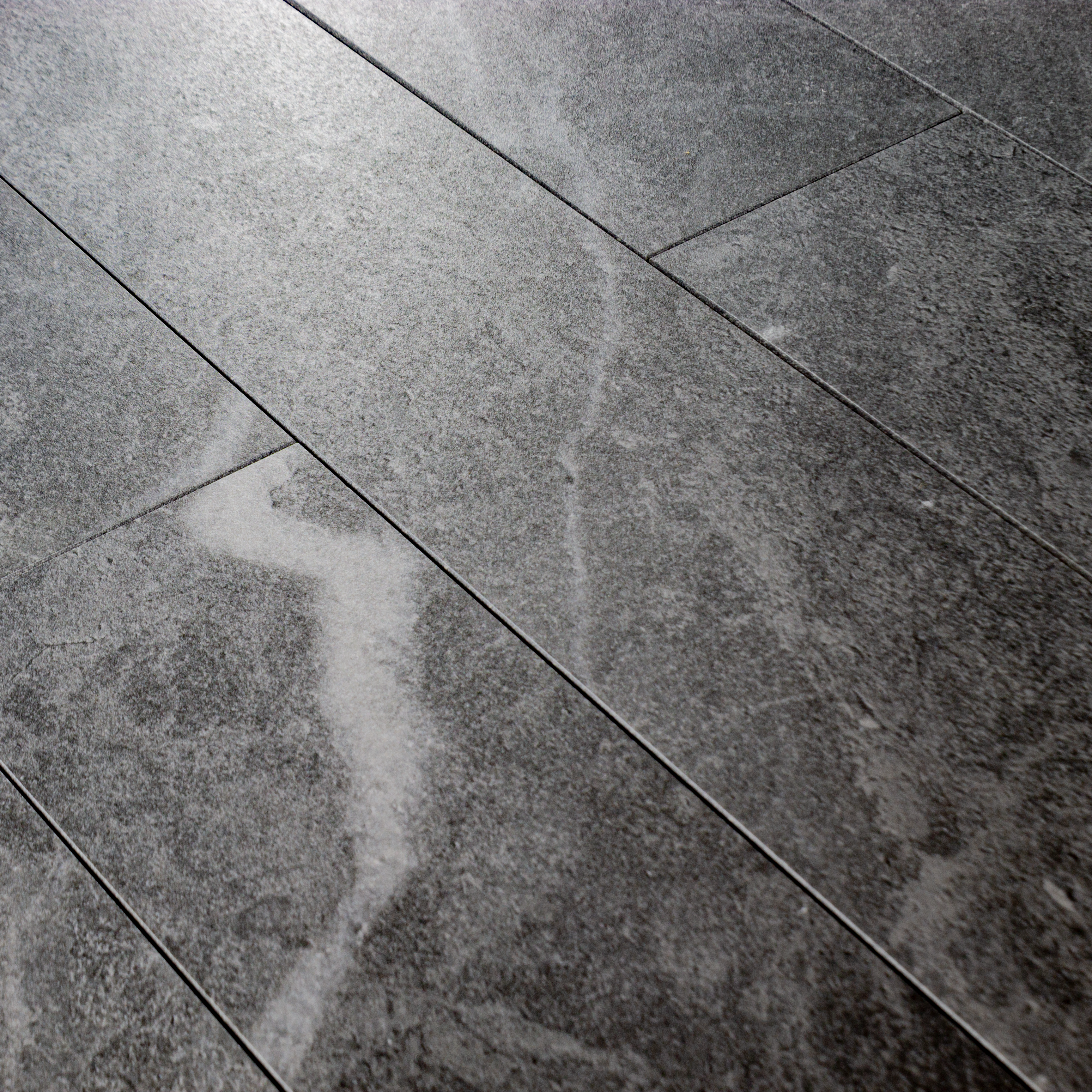 Angled close up of a group of 4x24 dark grey stone look tiles in a brick layout. 