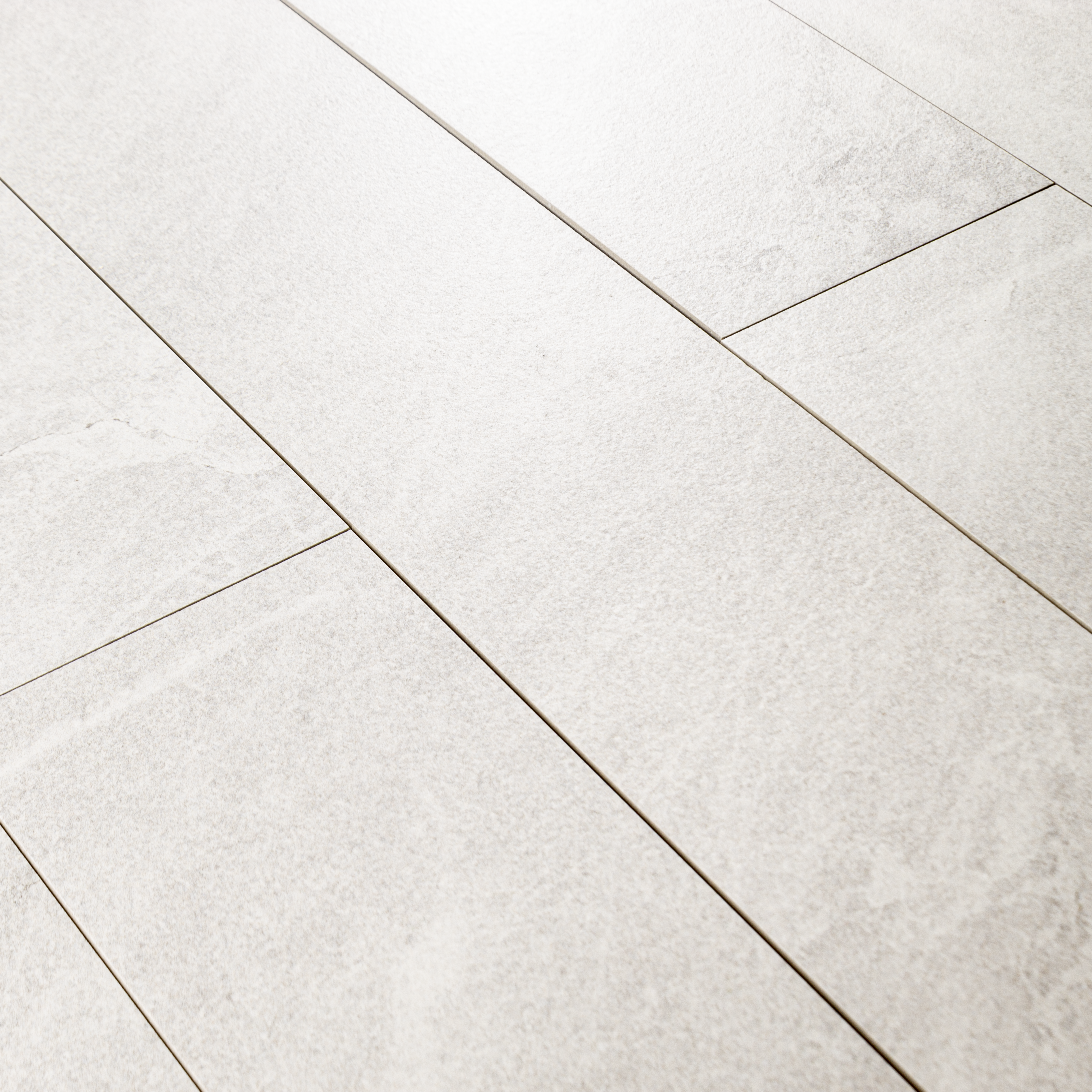 Angled close up view of a group of 4x24 snow white stone look tiles in a brick layout. 