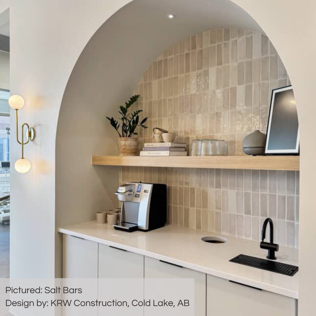 A stunning dental offices coffee nook nestled in an arched insert. the back wall is tiled with tilesinspired salt bars glossy variated subway tiles in a modern vertical stack. the tiles colours vary in whites, greys and greiges. with light grout and light counters and decor. 