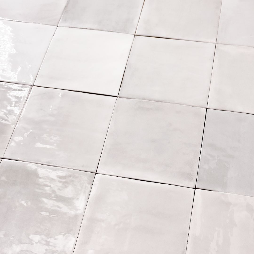 Ariel slightly tilted or angled view of a group of glossy 5x5 textured light grey zellige tiles showing the textured edges and colour variation. 