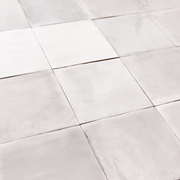Angled ariel view of a group of glossy 5x5 textured light grey zellige tiles showing the textured edges and colour variation. 